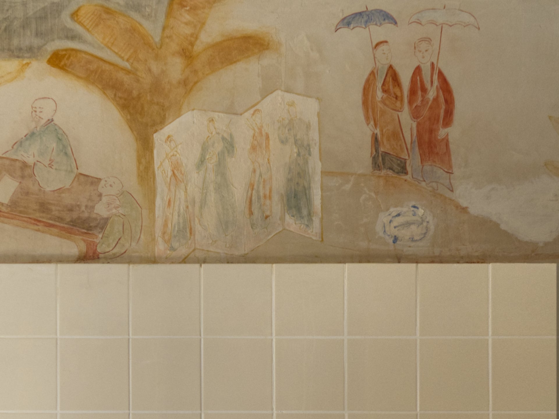 Decorative wall mural with people and a palm tree on a tiled wall.